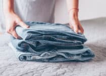 woman folds a jeans on grey cover on bed pile of 2021 09 02 14 44 46 utc 1