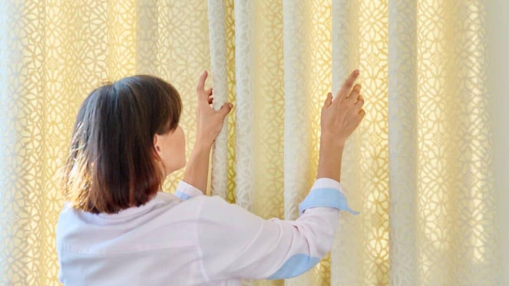 woman touches curtains lays out the folds on ligh 2022 07 15 16 16 35 utc